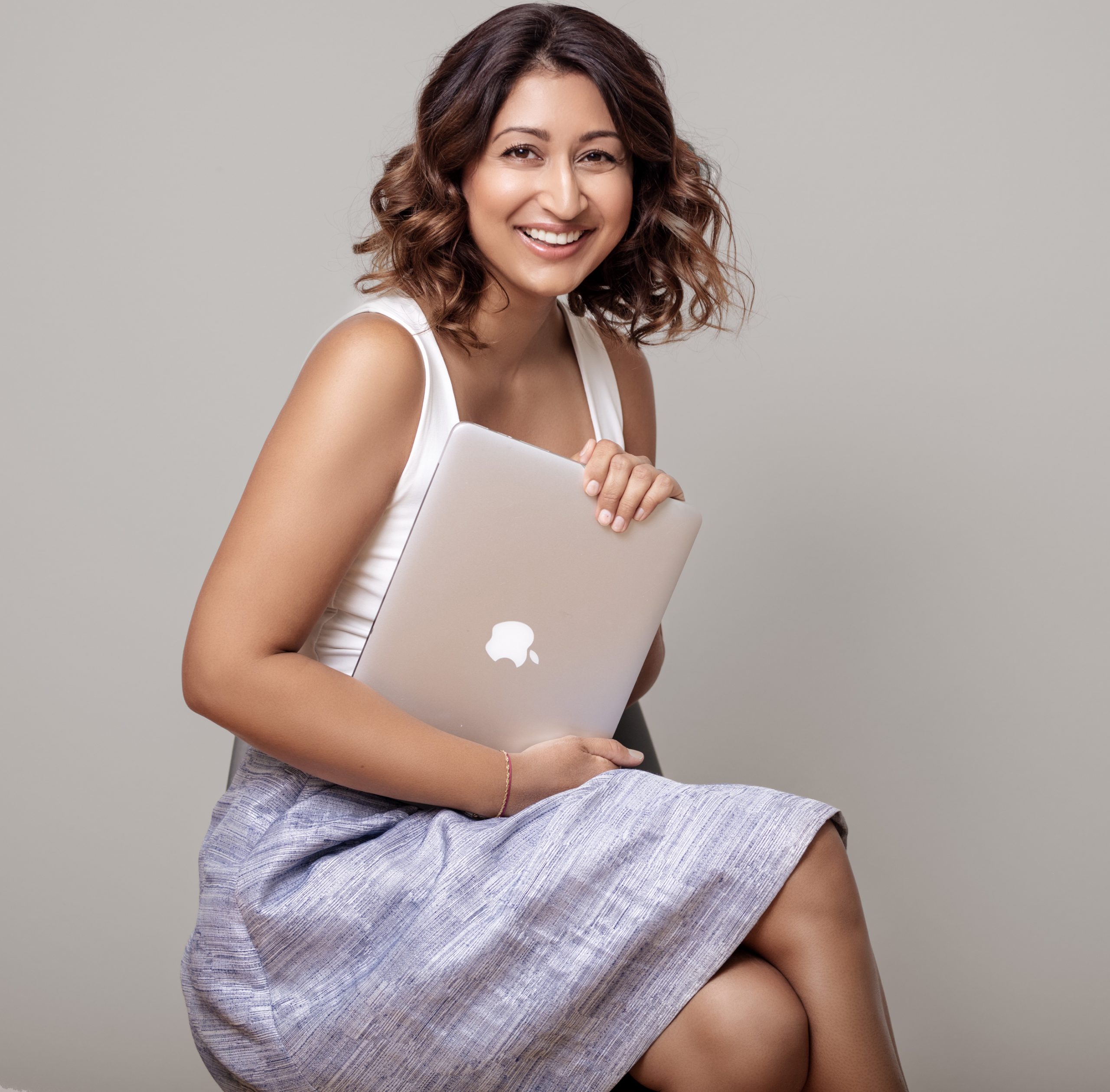 Mashaal Omary sitzt lächelnd auf einem Hocker und hält ihren Laptop