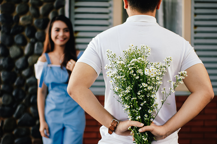 Mann versteckt Blumen hinter seinem Rücken für sein Date