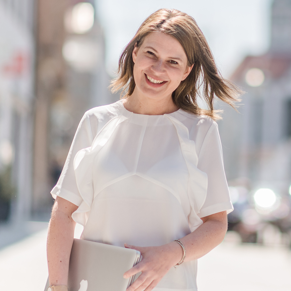 Bernadette hält einen Laptop in der Hand und lächelt in die Kamera