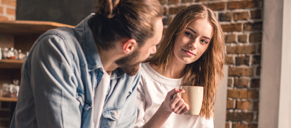 junges Pärchen sitzt mit Kaffee in der Hand in der Küche